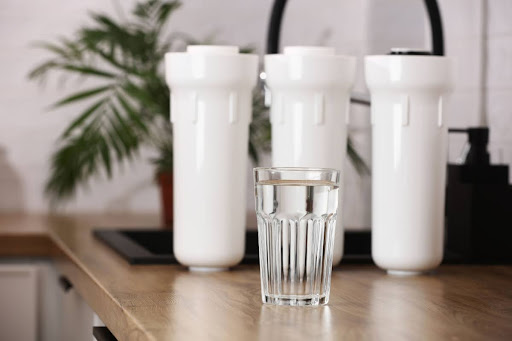 Glass of water positioned in front of water filtration system.