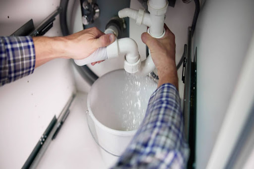 Hands holding P trap under the sink that's draining into a bucket.