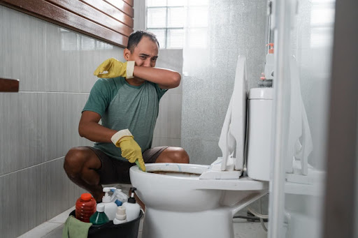 Homeowner covering nose while cleaning toilet.
