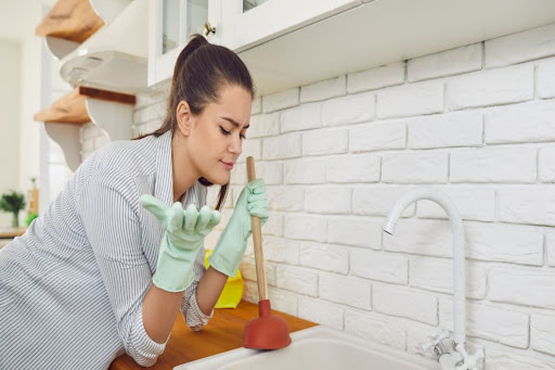 Homeowner using plunger to unclog kitchen sink.